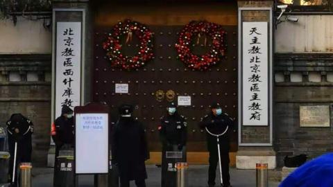 12月24日平安夜，网上传出的照片显示，北京一所天主教堂，一排手持防暴器械的警察守在门口，一块告示上写着暂停一切活动。网友嘲讽说，想过圣诞节，还得先过警察这一关。（网络图片）