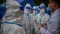 2020年6月22日在中国北京官方指定的COVID-19病毒核酸检测现场，一名戴着口罩的医生正向几位身穿防毒服的防疫工作人员发出指令。(Kevin Frayer/Getty Images)