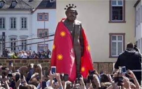 上图：讽刺图片：德国特里尔市中心广场的巨型马克思铜像戴上冠状病毒王冠、披上病毒红旗，市民们围在四周争相拍照。