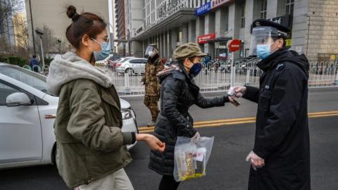 图为大陆社区治安员戴着防毒面具为民众测体温。（ Kevin Frayer/Getty Images)